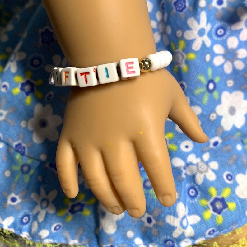 May include: White beaded bracelet with colorful letter beads spelling the name "FTIE".