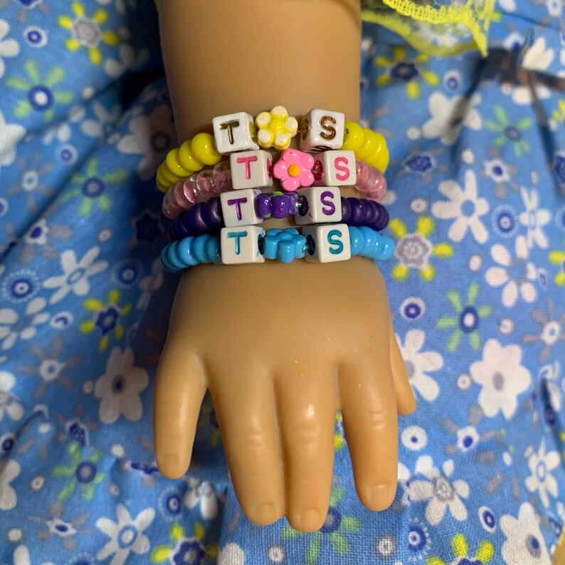 May include: A stack of colorful beaded bracelets with letter beads spelling out "TISS" and flower charms.