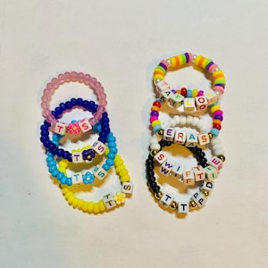 May include: A set of colorful beaded bracelets with letter beads spelling out words like "T.S.S", "SWIFT", "ERAS", and "TAYLOOR".