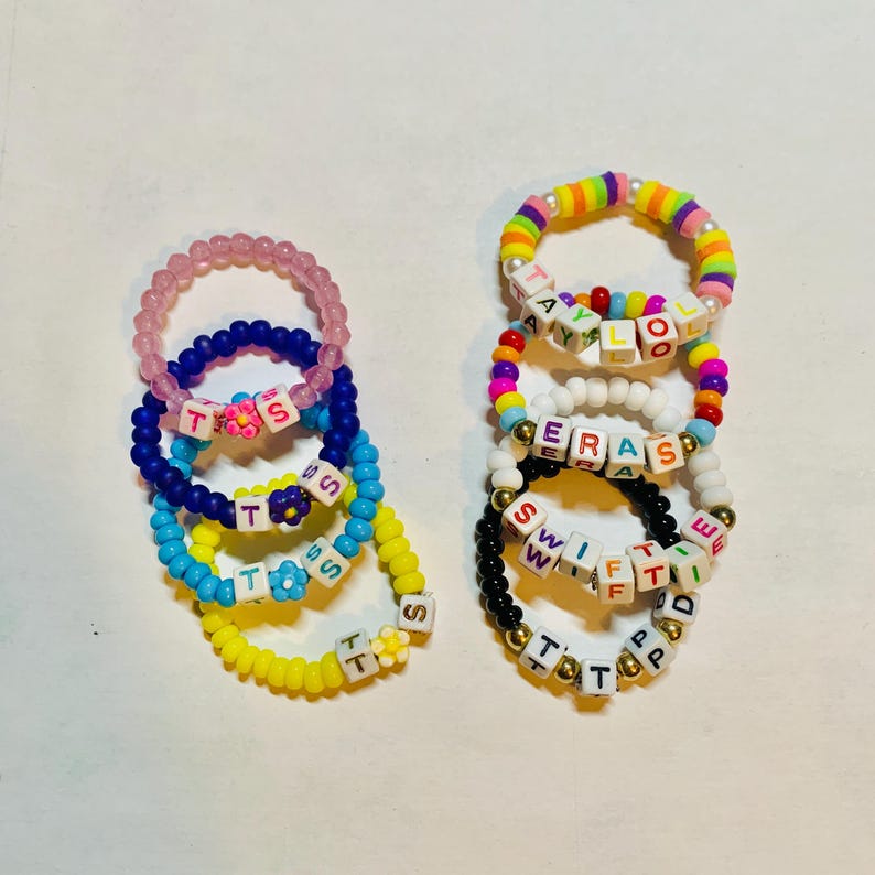 May include: A set of colorful beaded bracelets with letter beads spelling out words like "T.S.S", "SWIFT", "ERAS", and "TAYLOOR".