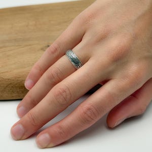 May include: A silver ring with an intricate Celtic knot design. The ring is worn on a finger, showcasing the detailed pattern and metallic sheen. The ring's design features interwoven lines and shapes.