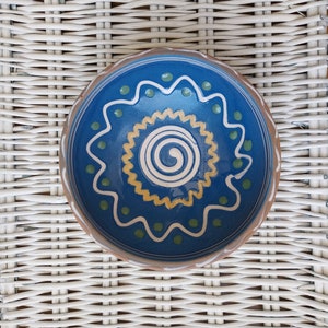 May include: A blue ceramic bowl with a yellow and green swirl design. The bowl is hand-painted and has a rustic, handmade look.