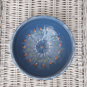 May include: A blue ceramic bowl with a white rim and a decorative design of orange dots and green and white swirls.