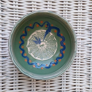 May include: A green ceramic bowl with a white and green swirl design and blue and orange accents.