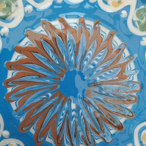 May include: A blue ceramic plate with a white and brown floral design. The plate has a glossy finish and is decorated with a swirling pattern.