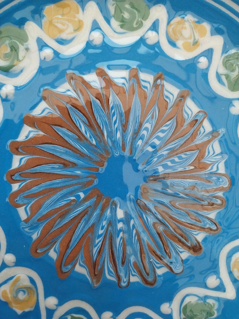 May include: A blue ceramic plate with a white and brown floral design. The plate has a glossy finish and is decorated with a swirling pattern.