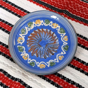 May include: A blue ceramic plate with a white, yellow, and green floral design. The plate has a brown center with a blue and white swirl pattern.