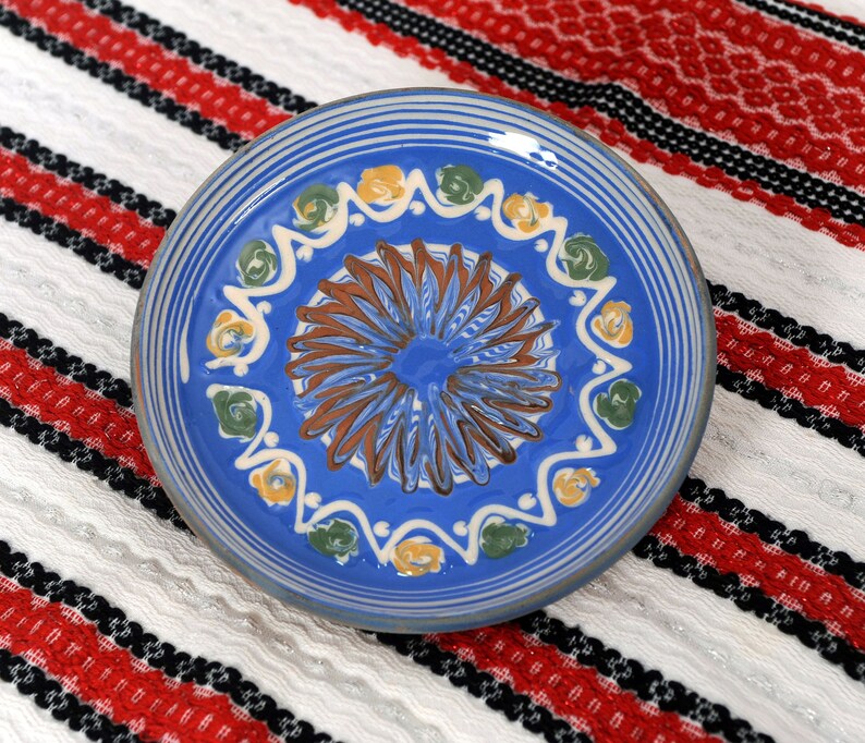 May include: A blue ceramic plate with a white, yellow, and green floral design. The plate has a brown center with a blue and white swirl pattern.