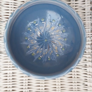 May include: A blue ceramic bowl with a white and yellow marbled design and green dots. The bowl is on a white wicker surface.