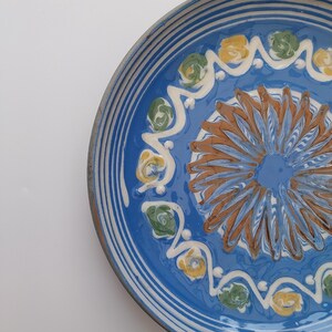 May include: A blue ceramic plate with a white rim and a decorative design of brown, yellow, and green swirls and flowers.