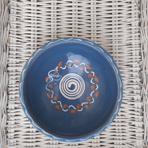 May include: A blue ceramic bowl with a white and orange swirl design. The bowl is sitting on a white wicker surface.