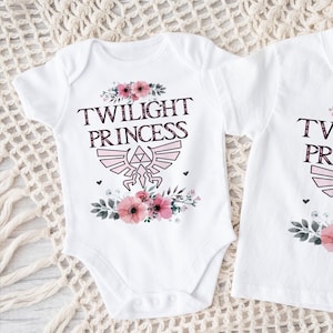 May include: Two white shirts with the text "Twilight Princess" in pink lettering, a pink floral design, and a stylized pink and white Triforce symbol.