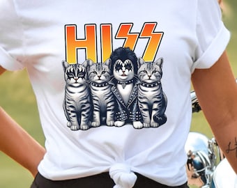 以下が含まれることがあります： オレンジと黄色の「HISS」の文字が入った、ロックバンド風の4匹の猫のグラフィックが特徴の白いTシャツ。猫はグレーと白の縞模様で、それぞれ特徴的なメイクとスタッズ付きの首輪をしています。
