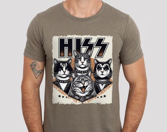 以下が含まれることがあります： KISSのバンドメンバーに扮した4匹の猫のグラフィックがプリントされた茶色のTシャツ。グラフィックには、バンド名の「KISS」が大きな黒文字で書かれており、猫の下には「Destroyer」と「Dynamite」の文字が書かれている。