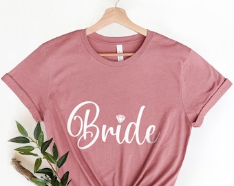 Puede incluir: Una camiseta rosa polvorienta con la palabra "Bride" en letras blancas cursivas con un pequeño diamante sobre la "i".