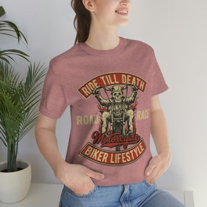 May include: A heather pink t-shirt with a graphic of a skeleton riding a motorcycle. The graphic includes the text "Ride Till Death", "Road", "Race", "Motorcycle", and "Biker Lifestyle".