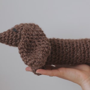 Könnte beinhalten: Ein braunes, gehäkeltes Dackel-Spielzeug. Das Spielzeug ist aus braunem Garn gefertigt und hat eine schwarze Nase.