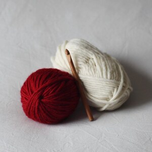 May include: Two balls of yarn, one red and one white, with a wooden crochet hook.