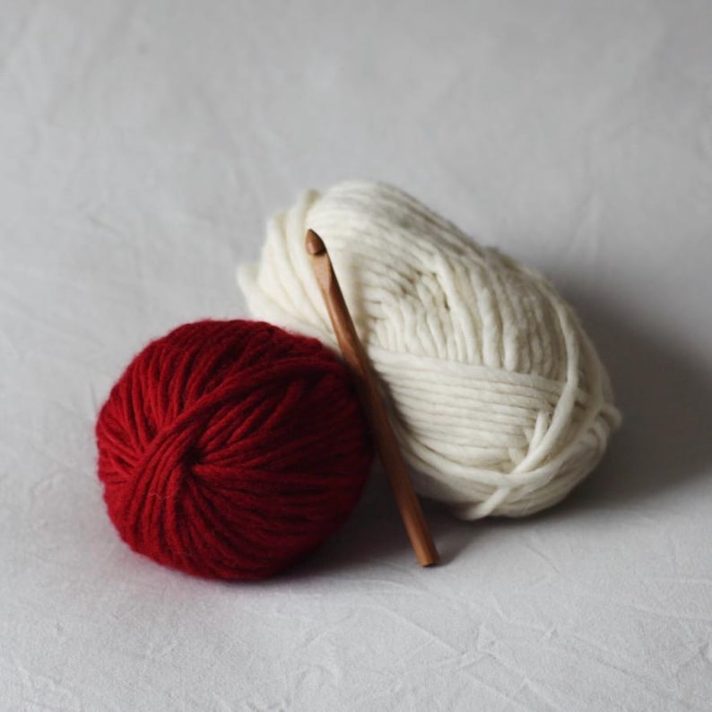 May include: Two balls of yarn, one red and one white, with a wooden crochet hook.