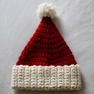 May include: A red and white crocheted Santa hat with a white pom-pom on top.