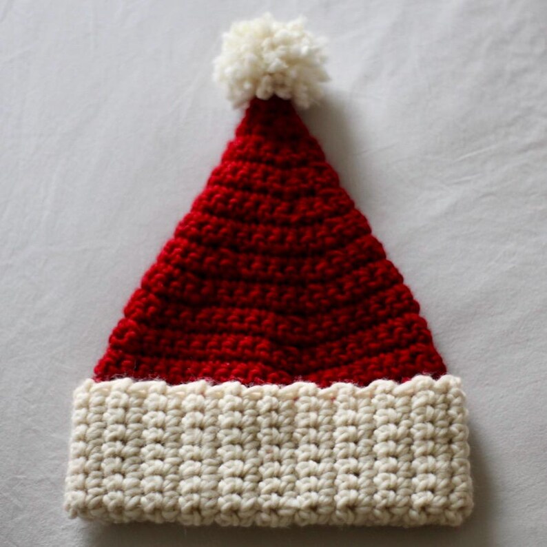 May include: A red and white crocheted Santa hat with a white pom-pom on top.