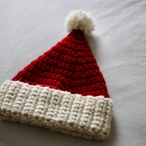May include: A red and white crocheted Santa hat with a white pom-pom on top.