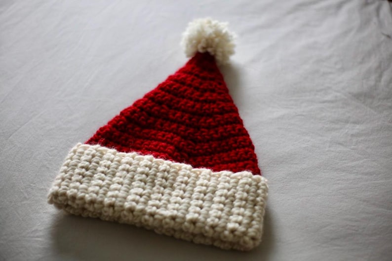 May include: A red and white crocheted Santa hat with a white pom-pom on top.
