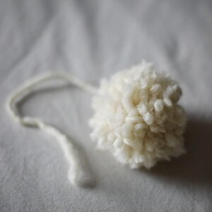 May include: A white fluffy pom-pom with a long white string attached.