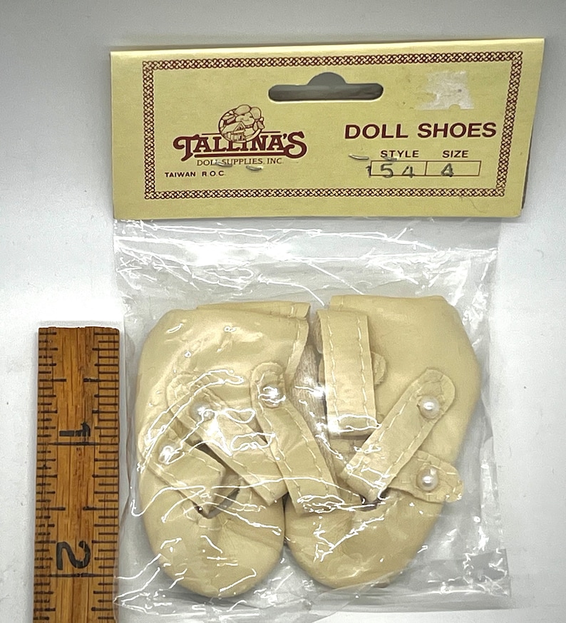 May include: A pair of white satin doll shoes with pearl accents. The shoes are packaged in a clear plastic bag with a label that reads "Tallina's Doll Supplies, Inc. Taiwan R.O.C." and "Doll Shoes Style 154 Size 4".