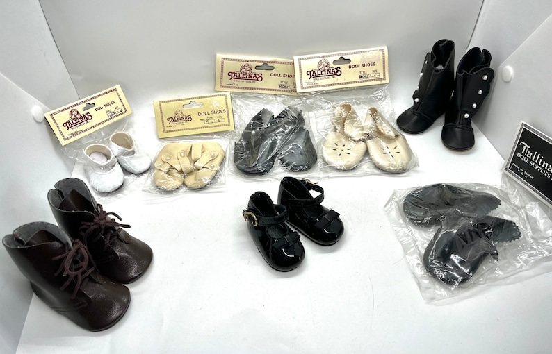 May include: Assortment of doll shoes in various styles and colors, including black leather boots, white canvas shoes, brown leather boots, and black patent leather shoes. The shoes are packaged in clear plastic bags with the brand name "Tallinas Doll Supplies" printed on the packaging.