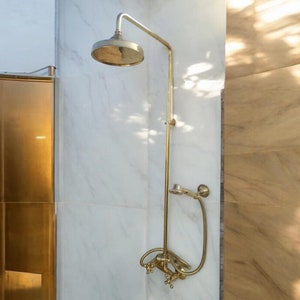 May include: A gold shower head with a handheld shower attachment, mounted on a white marble wall.