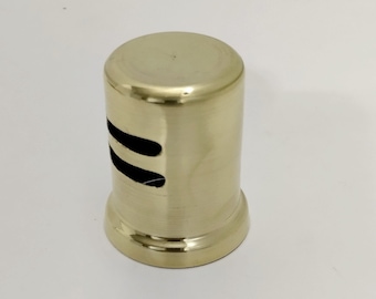 May include: A cylindrical, gold-colored metal object with two curved, black slits. The object has a slightly flared base and a rounded top. The surface appears smooth and reflective, suggesting a polished finish. The design is simple and modern.