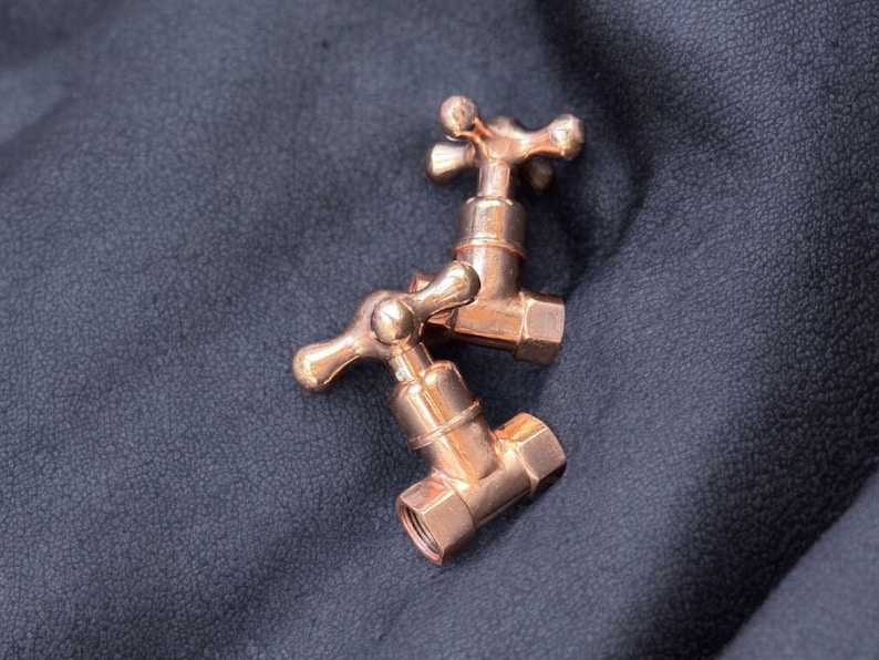 Peut inclure: Deux robinets d'eau en cuivre poli dot&eacute;s d'un design classique &agrave; poign&eacute;e en croix. Chaque robinet pr&eacute;sente une finition m&eacute;tallique r&eacute;fl&eacute;chissante avec un corps cylindrique et une base filet&eacute;e, affichant une teinte brun-rouge chaleureuse.