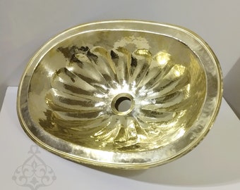 May include: A large, oval-shaped brass sink with a hammered finish and a decorative, scalloped design. The sink has a single drain hole in the center.