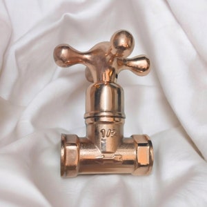 Peut inclure: Une vanne de robinet en m&eacute;tal cuivr&eacute; poli dot&eacute;e d'une poign&eacute;e en croix &agrave; quatre branches. Le corps central affiche le texte 1/2 et un symbole de fl&egrave;che indiquant le sens du flux. La vanne poss&egrave;de une base cylindrique avec des extr&eacute;mit&eacute;s hexagonales.