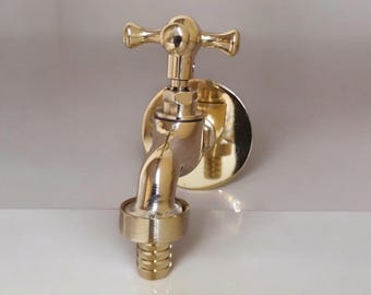 Puede incluir: Un grifo de latón pulido con un mango en forma de cruz y una placa trasera redonda. El grifo tiene un caño curvo y un extremo roscado para conectar una manguera. Diseñado para montaje en pared, tiene una apariencia clásica y elegante.
