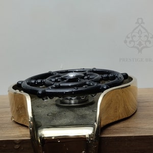 May include: A brass bottle stopper with a black, circular design. The stopper has a shiny, gold finish and a complex, geometric pattern. The brand name "PRESTIGE BRASS" is visible in the background.