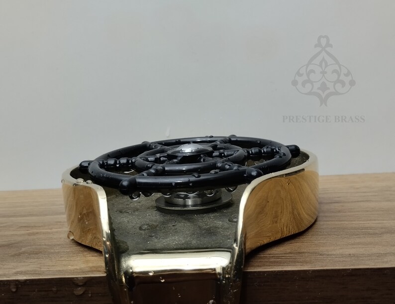 May include: A brass bottle stopper with a black, circular design. The stopper has a shiny, gold finish and a complex, geometric pattern. The brand name "PRESTIGE BRASS" is visible in the background.