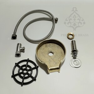 May include: A collection of plumbing components, featuring a brass soap dish, a flexible metal hose, and a black plastic wheel. Other parts include a T-fitting, a threaded rod, and washers. The text "PRECISE BRASS" is visible.