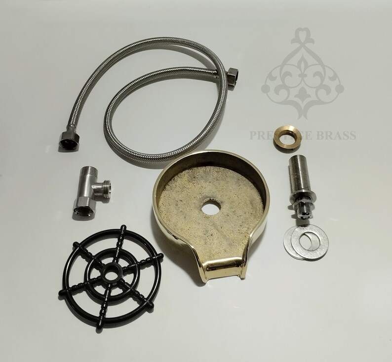 May include: A collection of plumbing components, featuring a brass soap dish, a flexible metal hose, and a black plastic wheel. Other parts include a T-fitting, a threaded rod, and washers. The text "PRECISE BRASS" is visible.