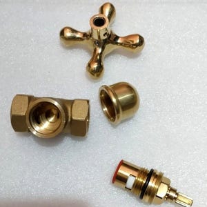 Peut inclure: Un ensemble de poign&eacute;e de robinet dor&eacute; comprenant une poign&eacute;e en croix &agrave; quatre branches, un corps de vanne cylindrique avec filetage interne, un capuchon bomb&eacute; lisse et une cartouche de vanne en laiton avec un joint rouge et un joint torique noir.