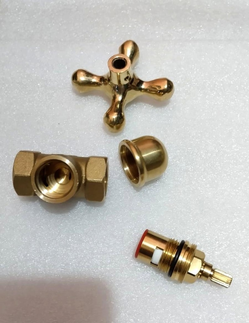 Peut inclure: Un ensemble de poign&eacute;e de robinet dor&eacute; comprenant une poign&eacute;e en croix &agrave; quatre branches, un corps de vanne cylindrique avec filetage interne, un capuchon bomb&eacute; lisse et une cartouche de vanne en laiton avec un joint rouge et un joint torique noir.