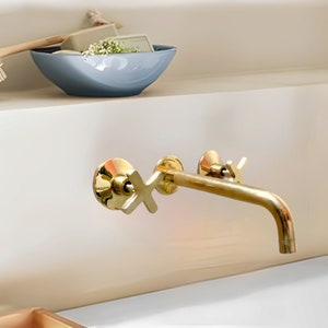 May include: A gold-toned bathroom faucet with a single handle and a curved spout. The faucet is mounted on a white wall.