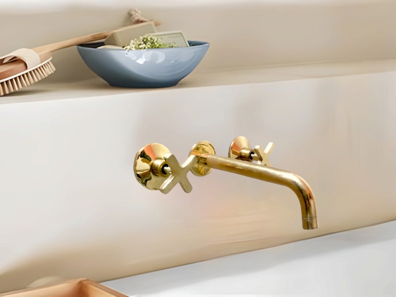 May include: A gold-toned bathroom faucet with a single handle and a curved spout. The faucet is mounted on a white wall.