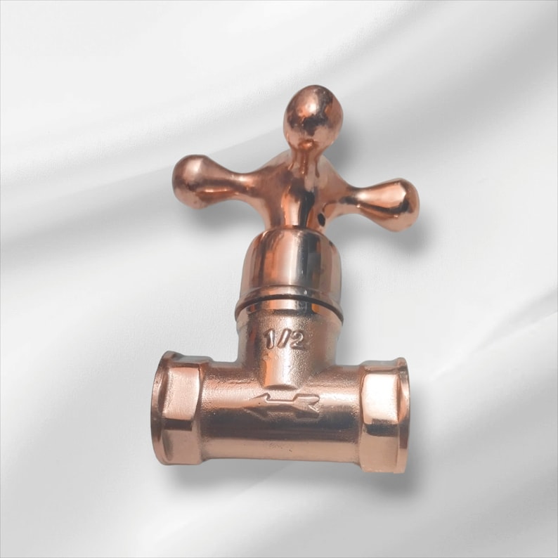 Peut inclure: Une vanne en m&eacute;tal de couleur cuivre poli dot&eacute;e d'une poign&eacute;e en forme de croix et d'un corps en T. La partie centrale de la vanne est grav&eacute;e avec le texte 1/2 et une fl&egrave;che indiquant le sens du flux, avec des extr&eacute;mit&eacute;s filet&eacute;es.