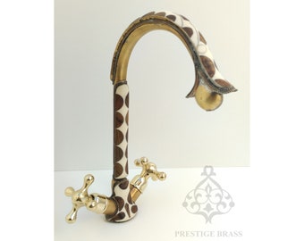 May include: A gold-toned faucet with a white and brown patterned design. The faucet has a curved spout and two handles. The faucet is labeled "PRESTIGE BRASS".
