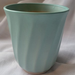 May include: A light blue ceramic planter with a fluted design. The planter is sitting on a white fabric surface.