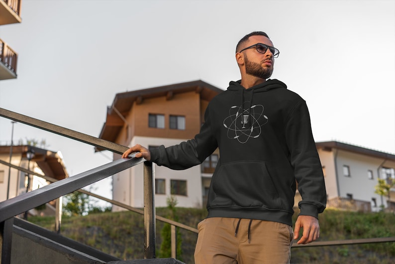 May include: A black hoodie with a white graphic of a microphone inside an atom symbol. The person wearing the hoodie is standing on a set of stairs.