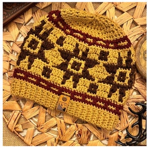 May include: A crocheted beanie hat in a mustard yellow colour with a brown and burgundy geometric pattern. The hat has a leather patch with a logo on the side.