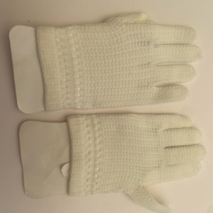 May include: A pair of white gloves. The gloves are made of a knitted material with a textured appearance. Each glove has a white cuff and a detailed pattern near the wrist. The gloves are designed for hand protection and warmth.